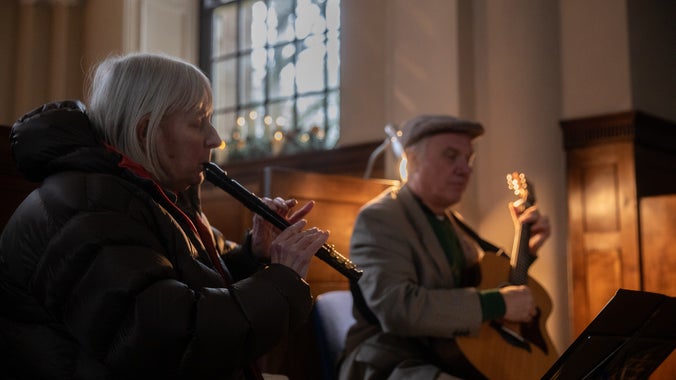 A woman playing recorder and a man playing guitar in soft lighting.